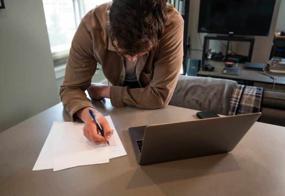Person filling out health insurance enrollment paperwork next to a laptop at home
