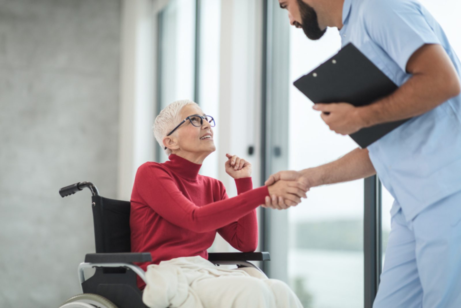 Smiling caregiver shaking hands with an older woman in a wheelchair, representing long-term care planning